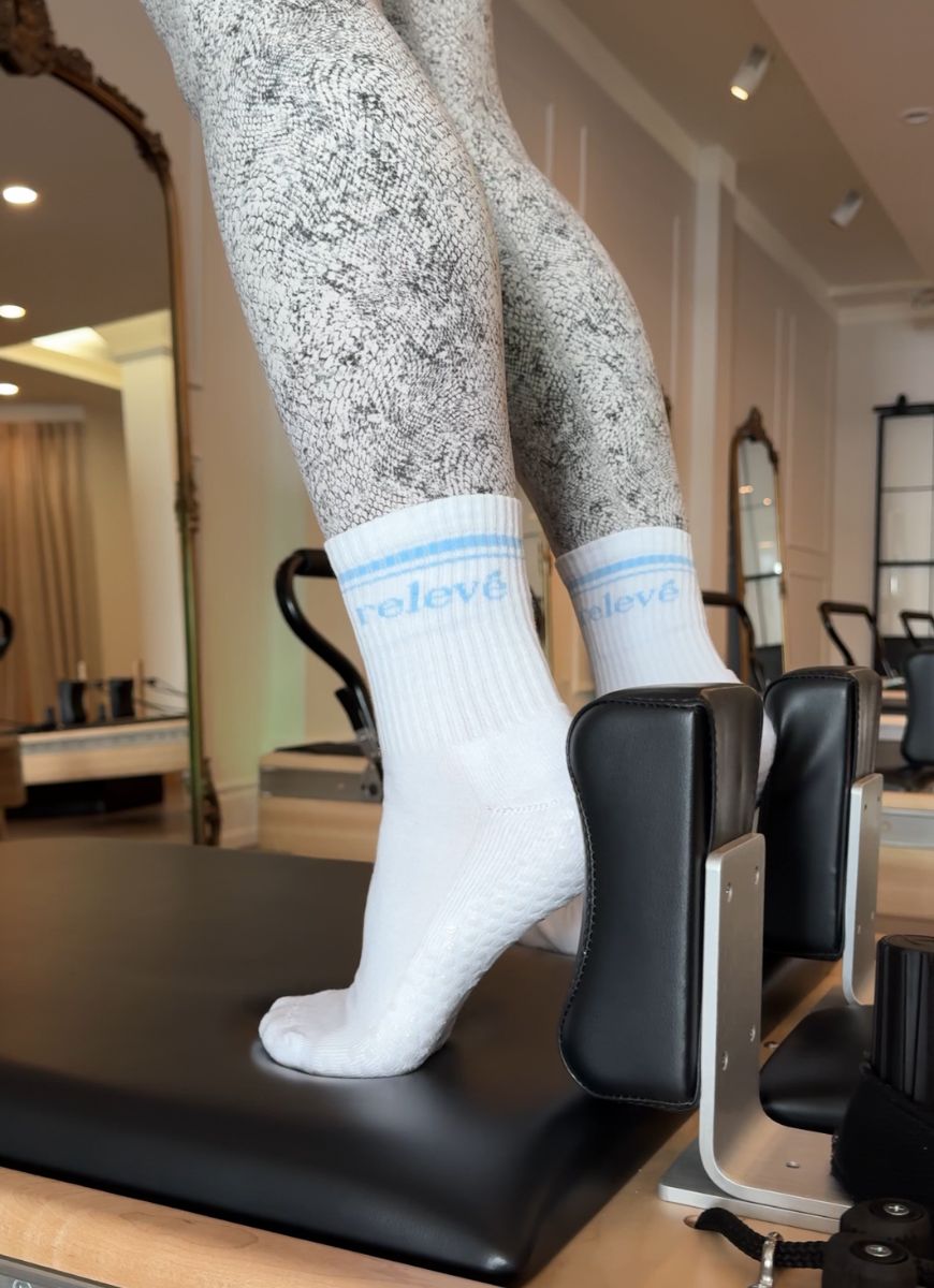 relevé Grip Socks in White with Blue Logo Shown on a Reformer Machine