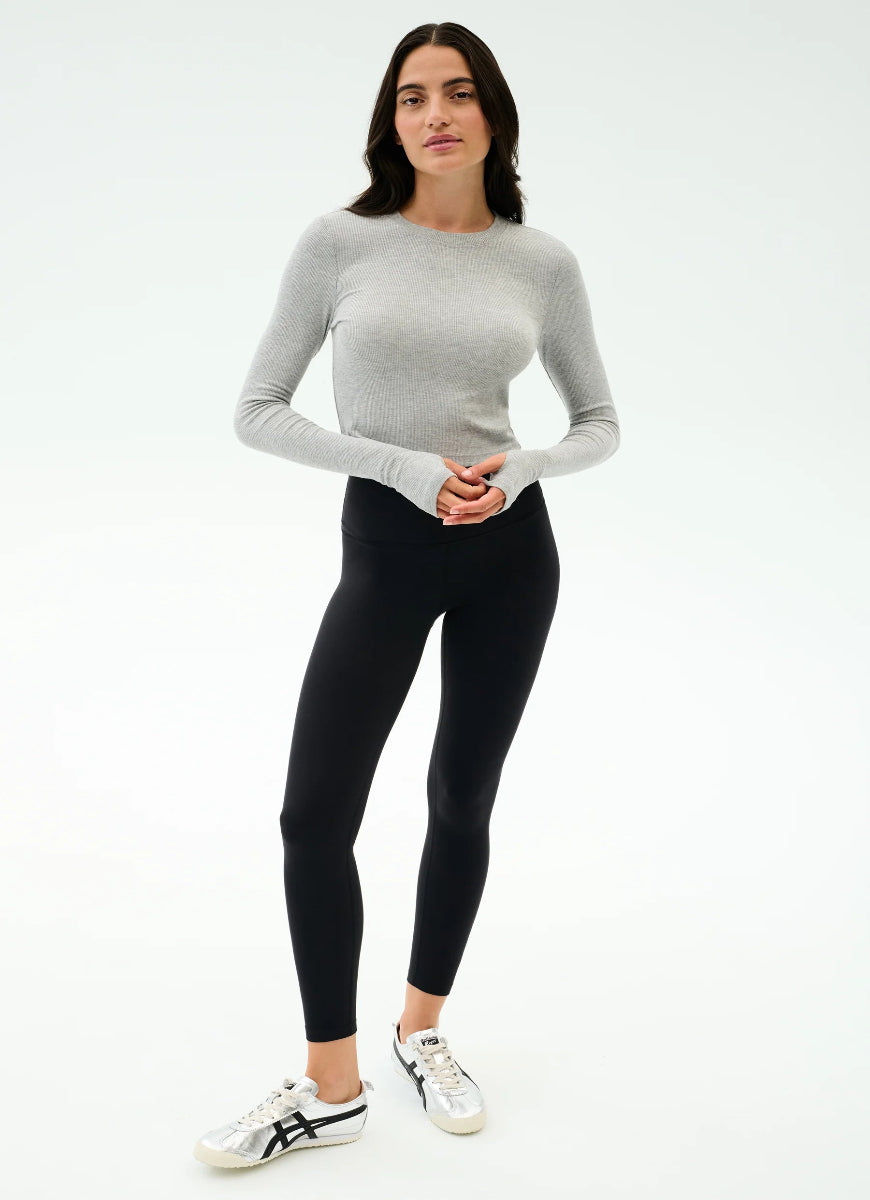 Woman wearing a gray long-sleeve top and black leggings on a white background