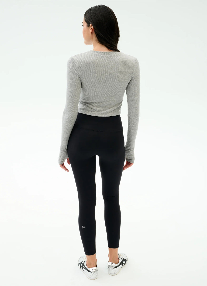Person wearing a gray long-sleeve top and black leggings on a white background