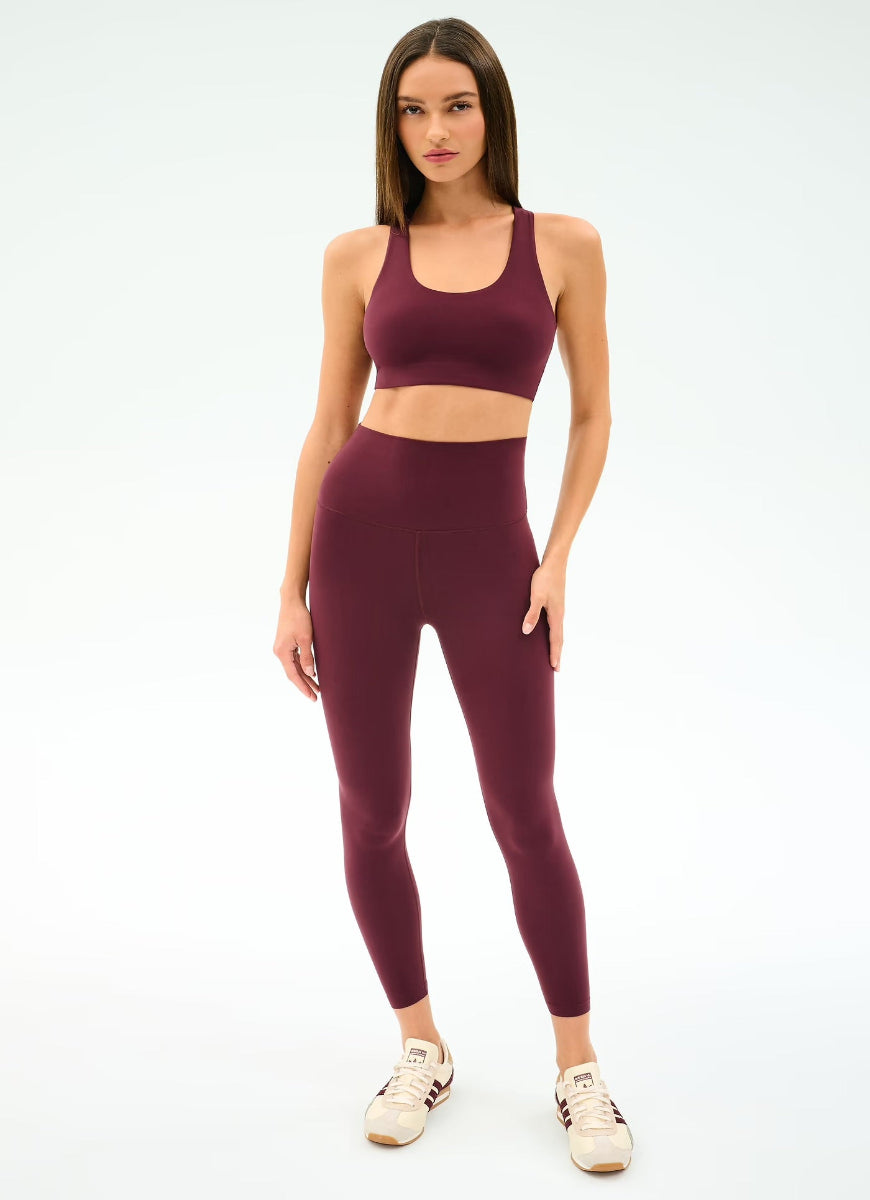 Woman wearing a maroon sports bra and leggings set on a white background