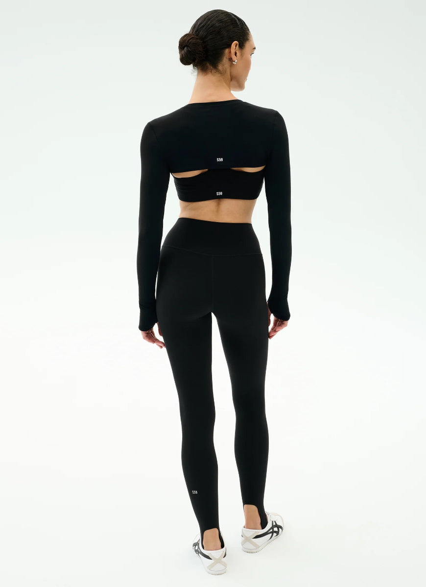 Person wearing a black long-sleeve crop top and leggings on a white background