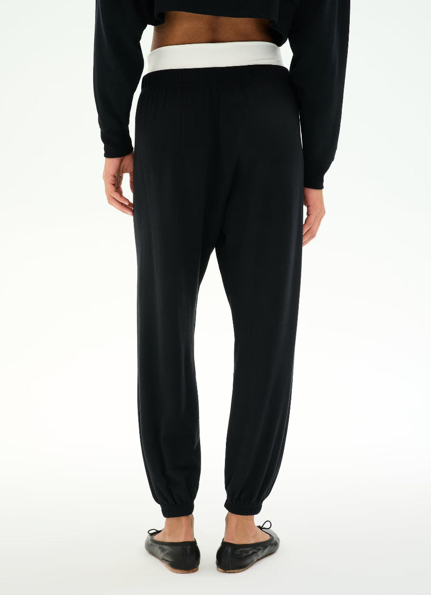 Black jogger pants with a contrasting white waistband, shown from the back on a model wearing a black crop top and black flats.