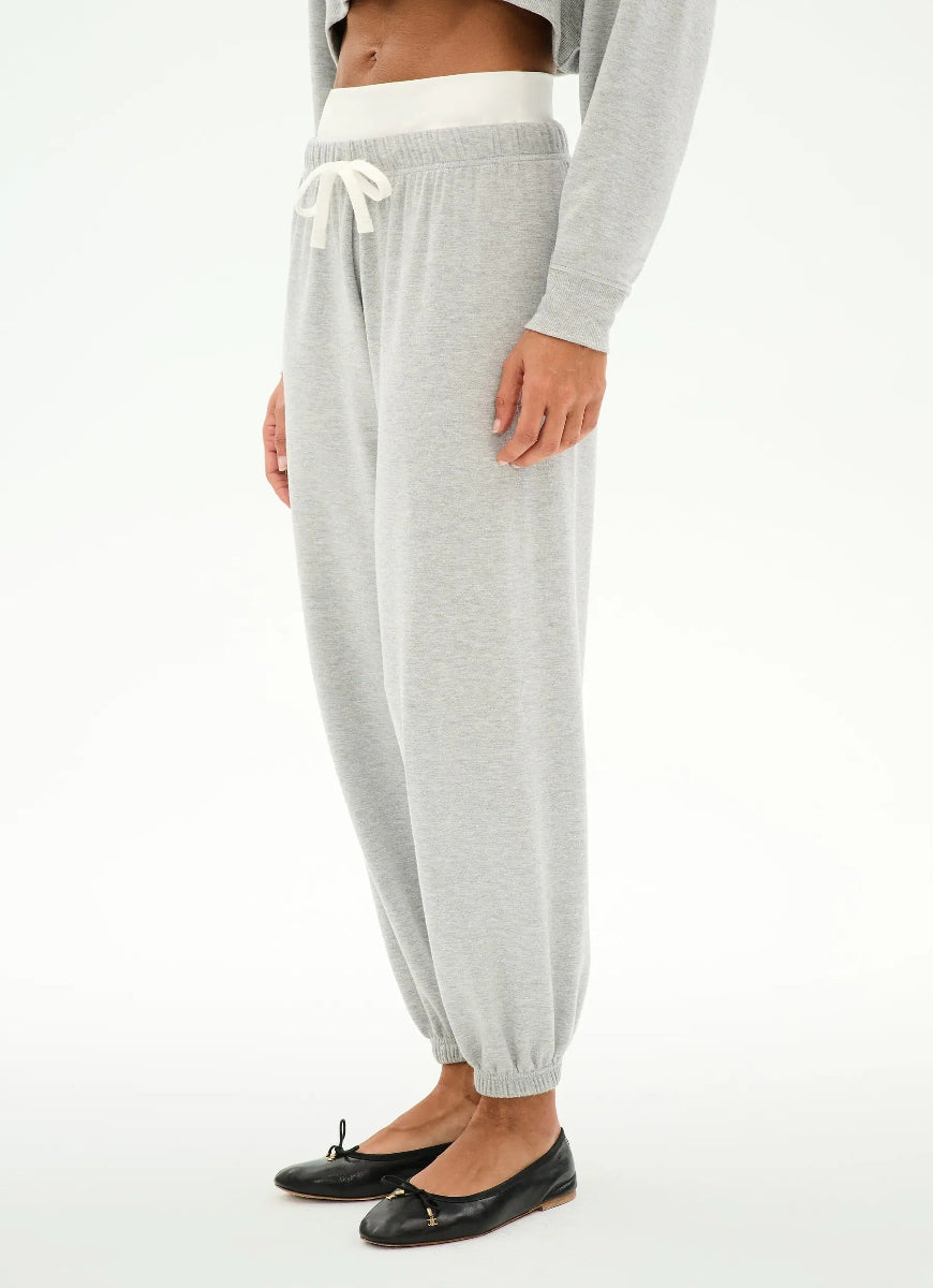 A person wearing light gray jogger sweatpants with a white drawstring and white elastic waistband, paired with black flats, photographed against a clean white studio background.