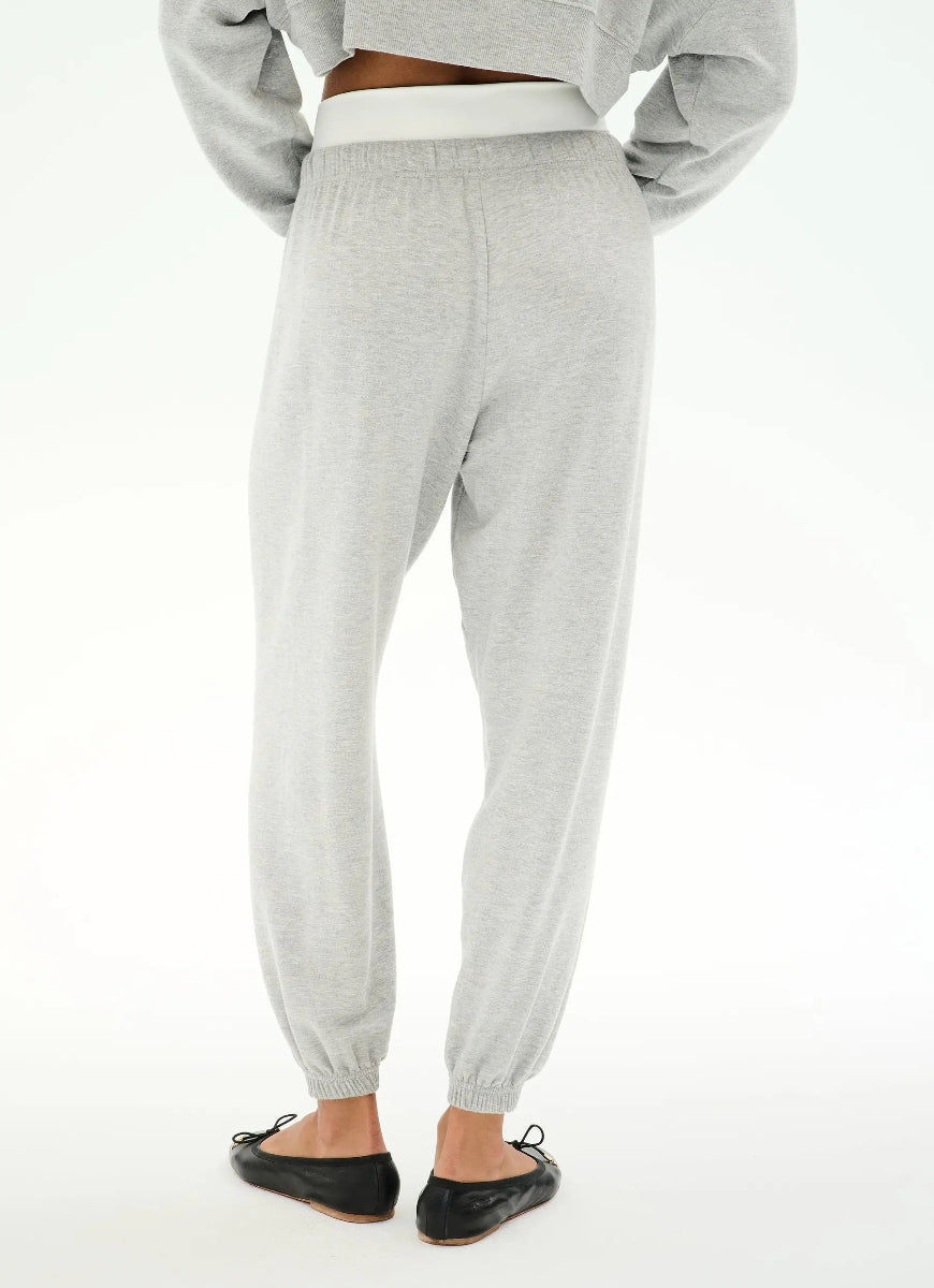 A person shown from the back wearing light heather gray jogger sweatpants with an elastic waistband and elastic ankle cuffs, paired with black flats against a plain white studio background.