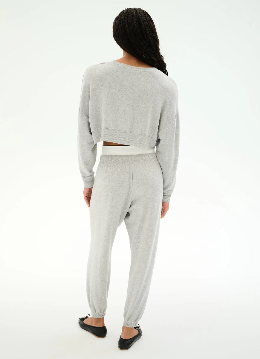 A woman shown from the back wearing a light gray heather cropped long-sleeve top and matching jogger pants, paired with black flats, against a plain white studio background.