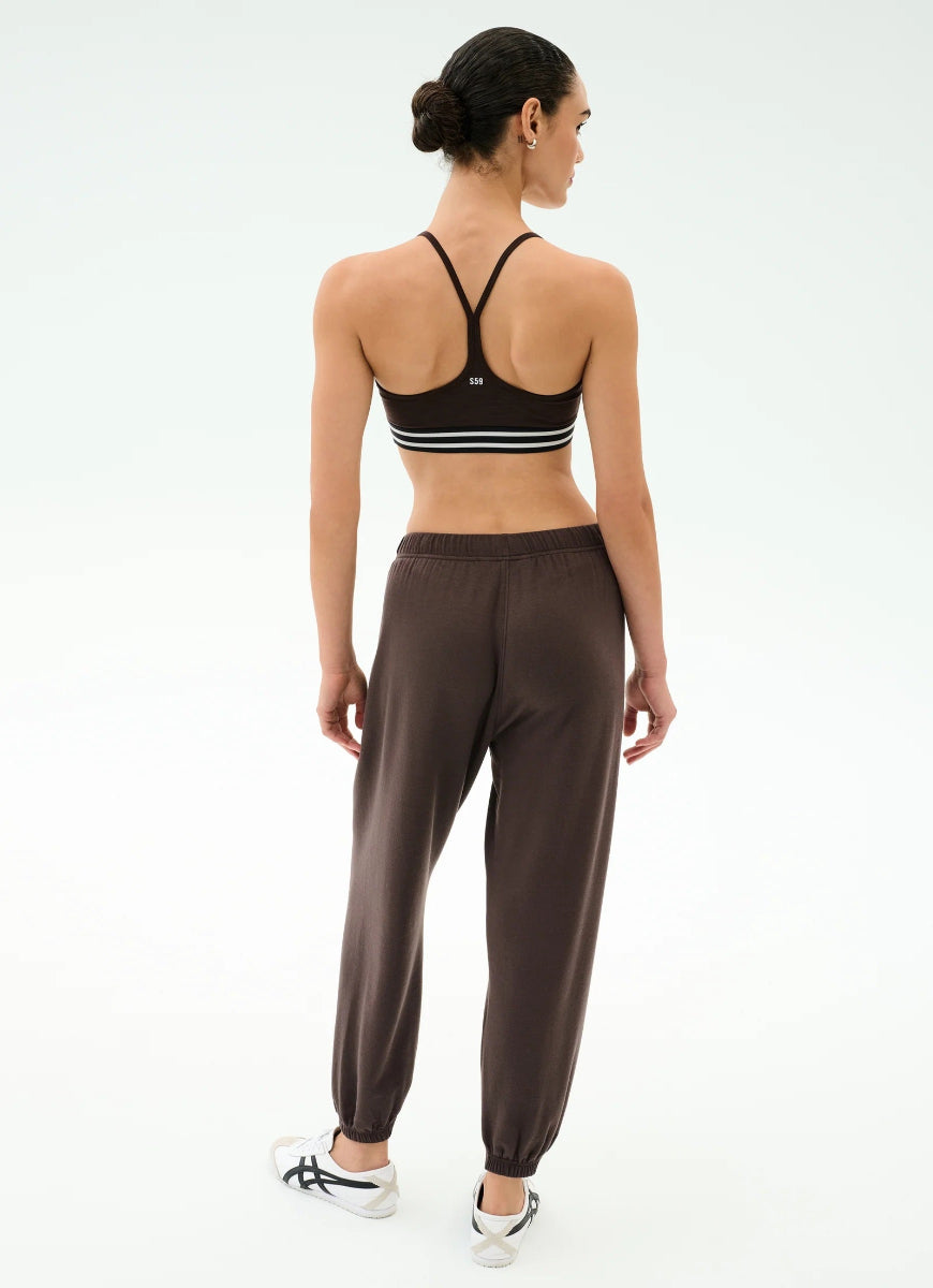 Woman wearing a black sports bra and brown jogger pants on a white background