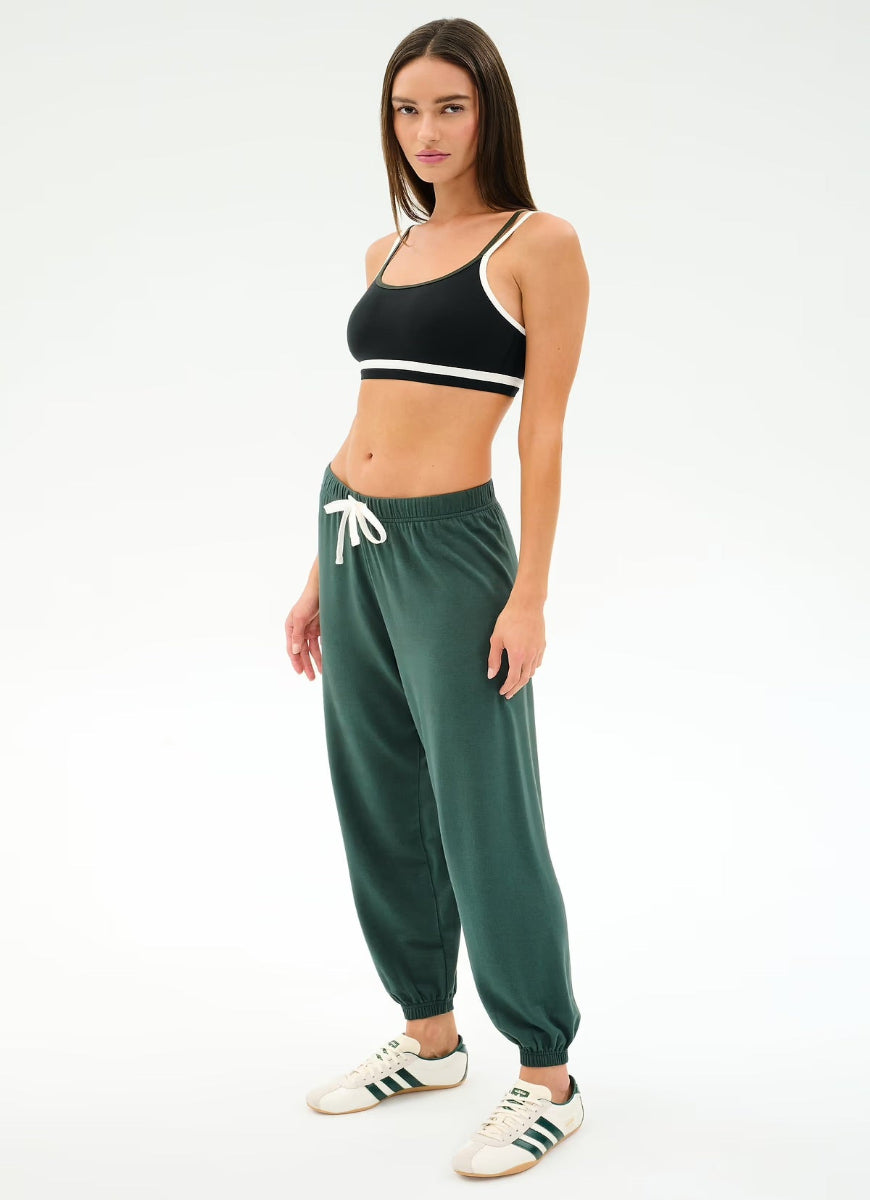 Woman wearing a black sports bra and green jogger pants on a white background