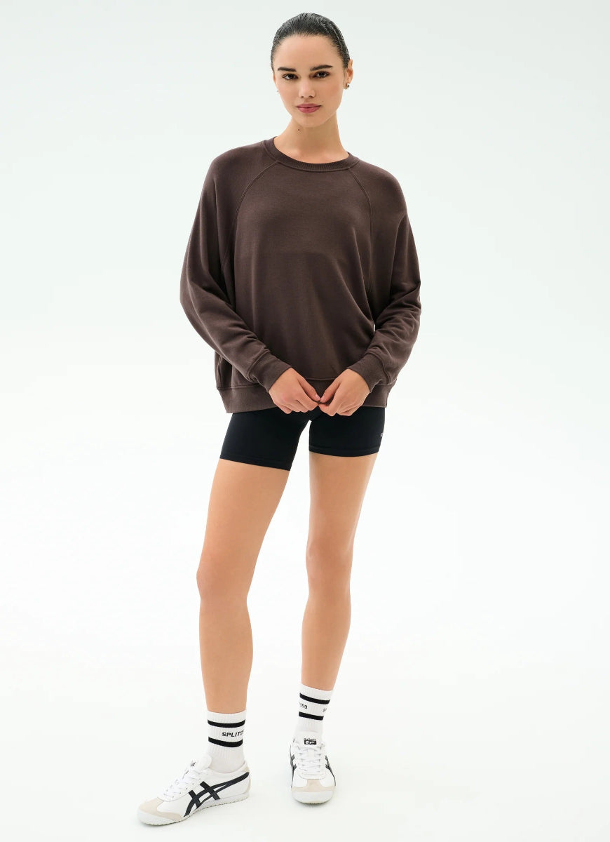 Person wearing a brown oversized sweater, black shorts, and white sneakers on a white background