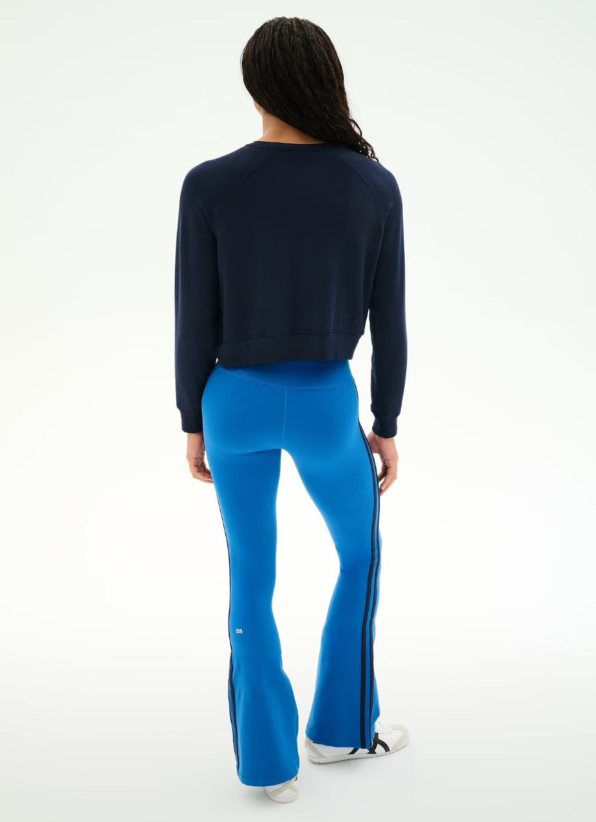 A model shown from the back wearing a dark navy cropped long-sleeve top and bright blue flared pants with black side stripes, against a plain white studio background.