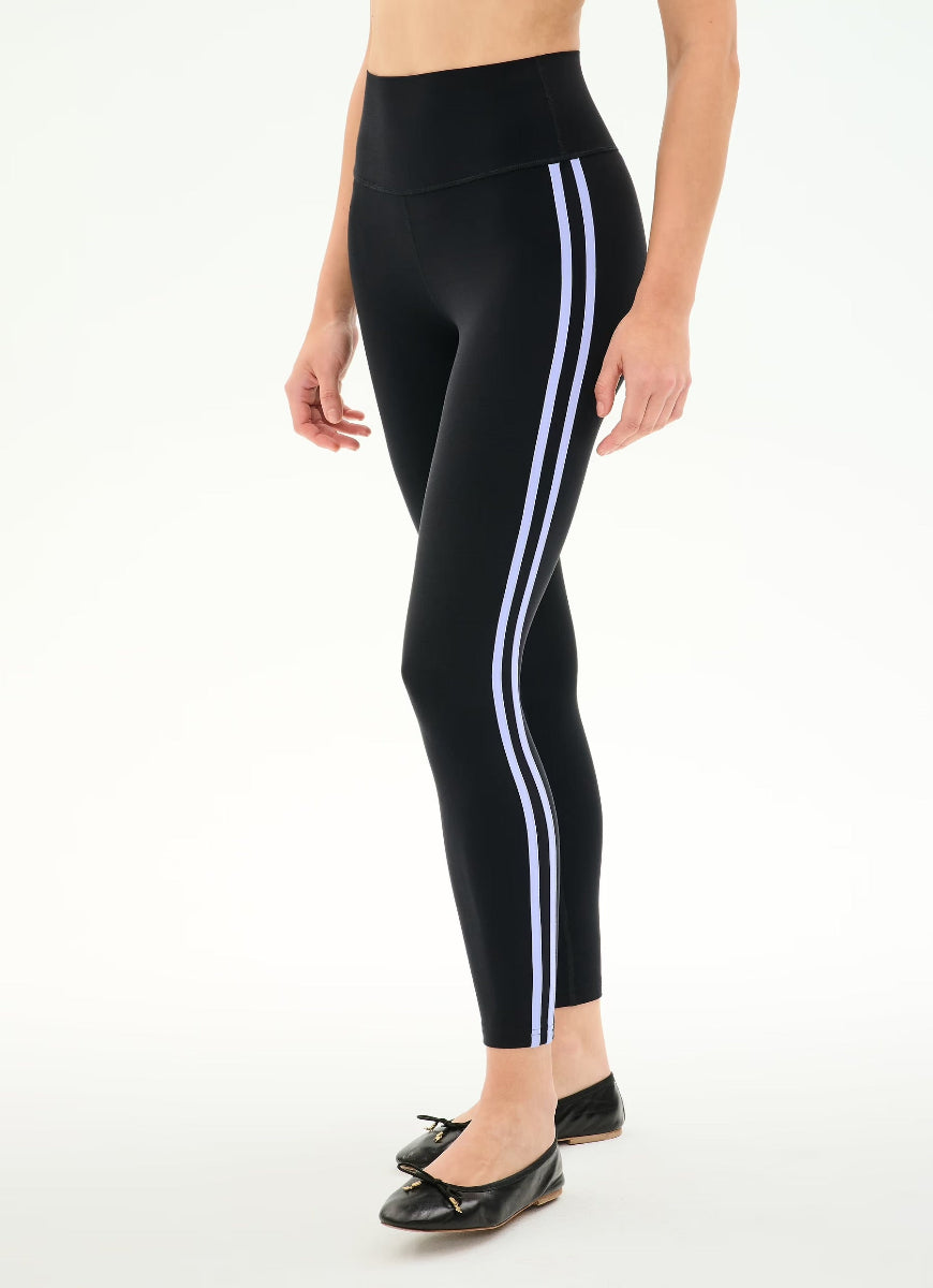 A model wearing black high-waisted leggings with two white side stripes, paired with black flat shoes, shown against a plain white studio background.