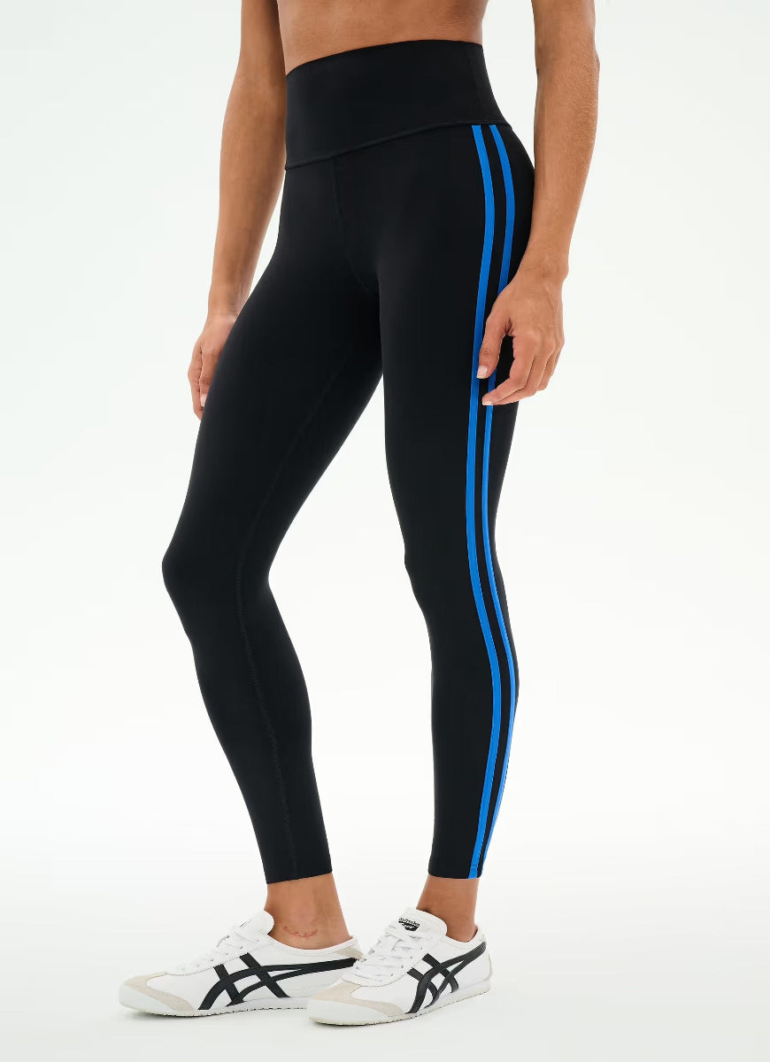 Black high-waisted leggings with two bright blue side stripes, modeled on a person wearing white sneakers against a plain white studio background.