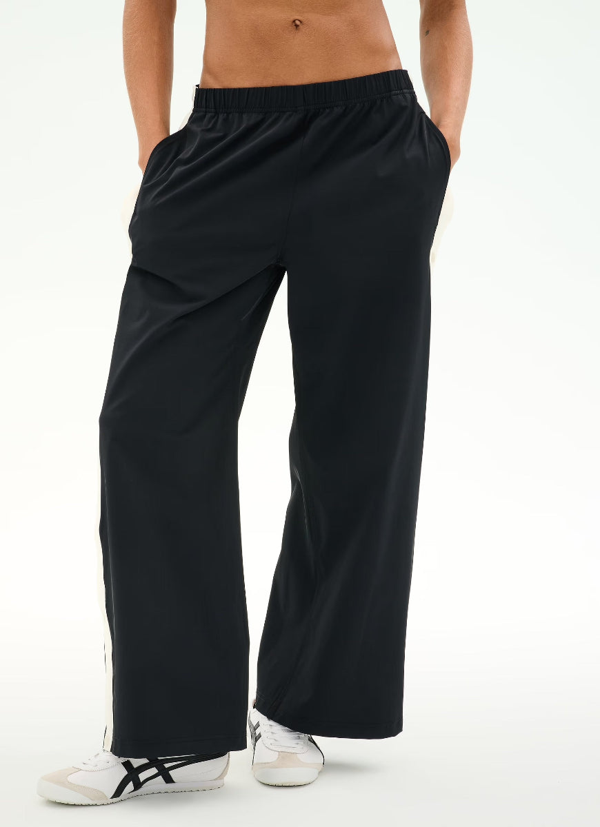 A person wearing black wide-leg athletic pants with white sneakers, shown from the waist down against a clean white studio background.