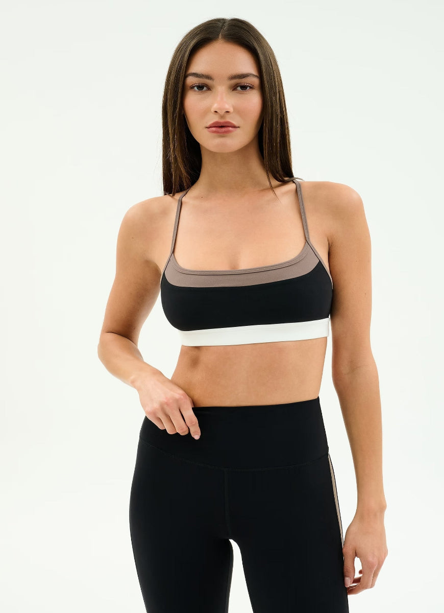 Woman wearing a black and white sports bra with a beige mesh panel on a white background