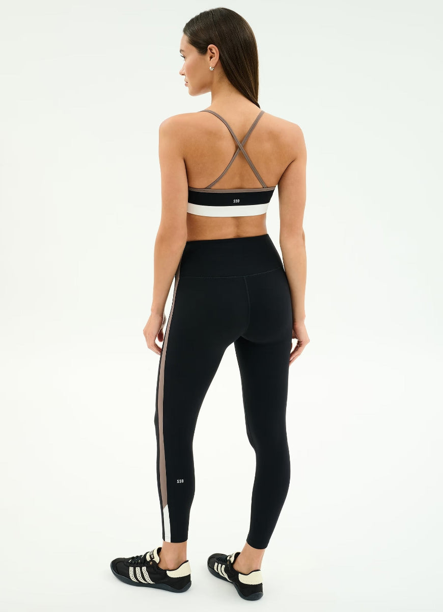 Woman wearing a black sports bra and leggings with white stripes on a white background