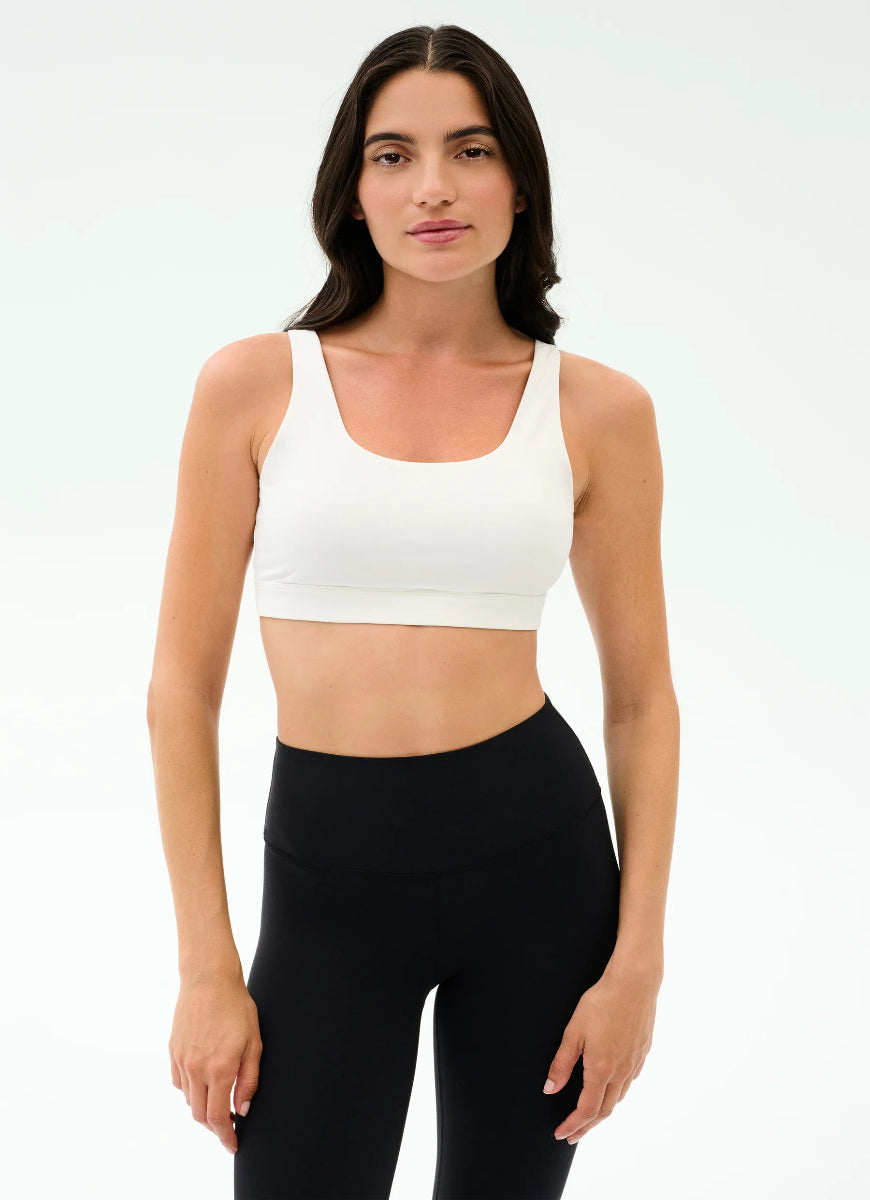 Woman wearing a white sports bra and black leggings on a light gray background