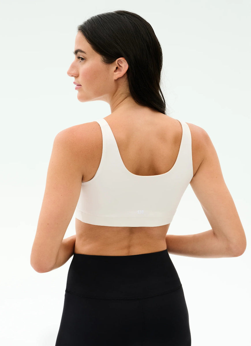 Woman wearing a white sports bra and black leggings on a light gray background