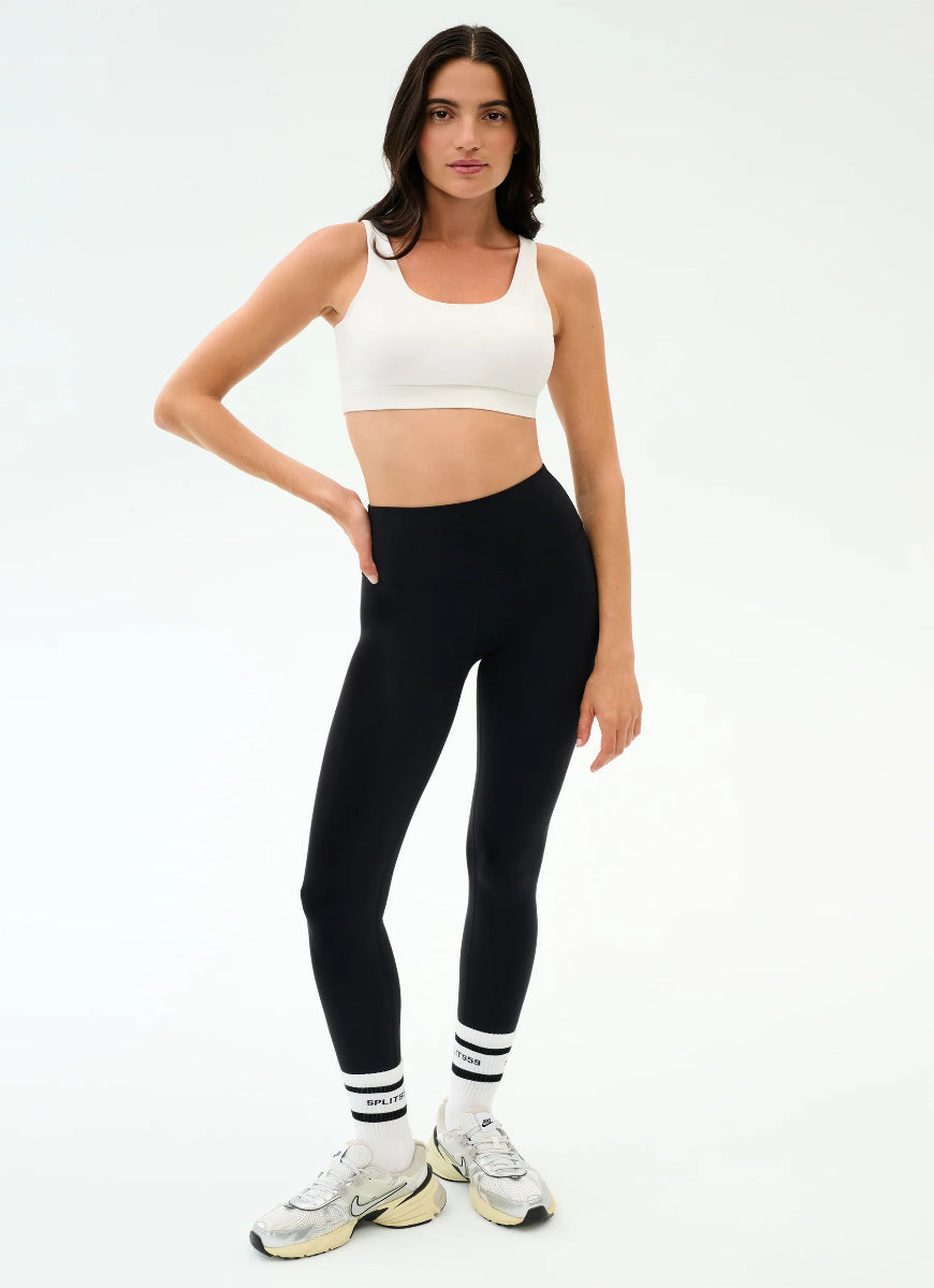 Woman wearing a white sports bra and black leggings on a white background