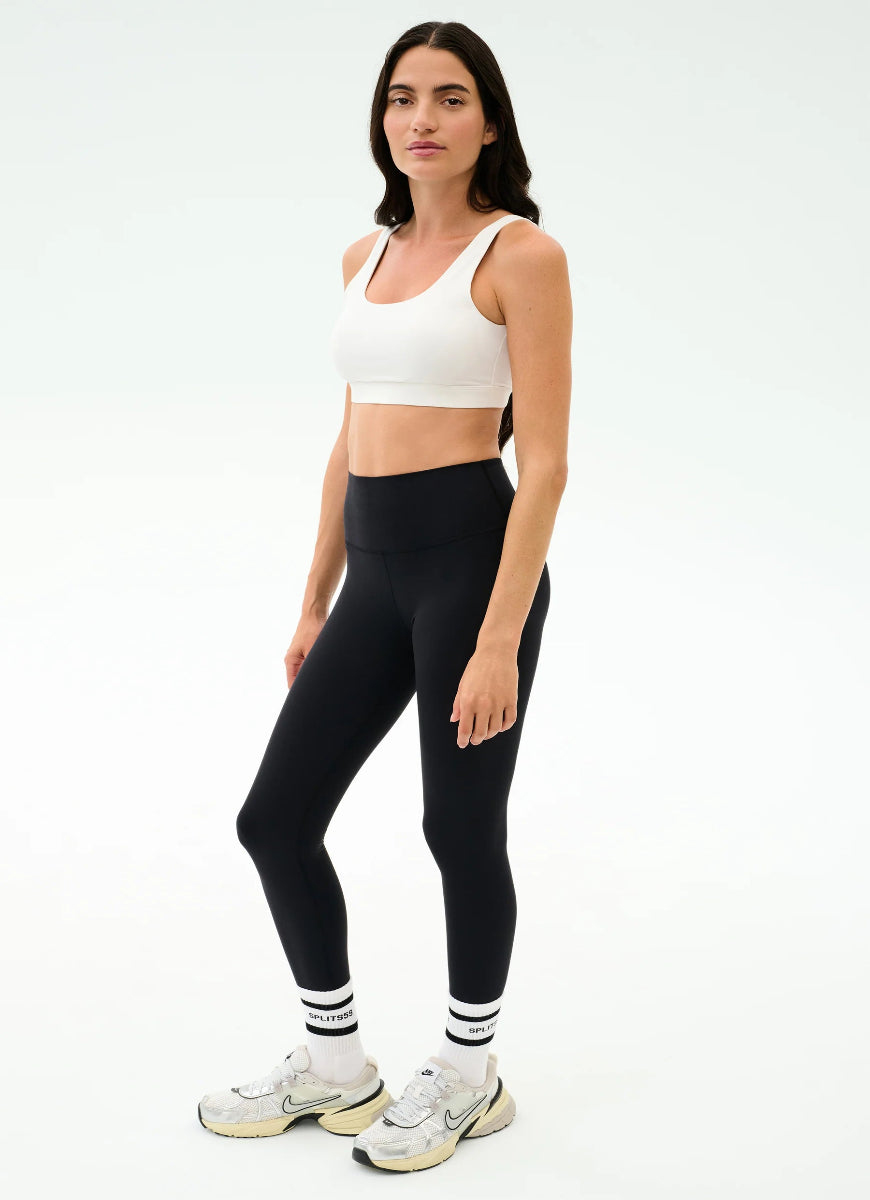 Woman wearing a white sports bra and black leggings on a white background