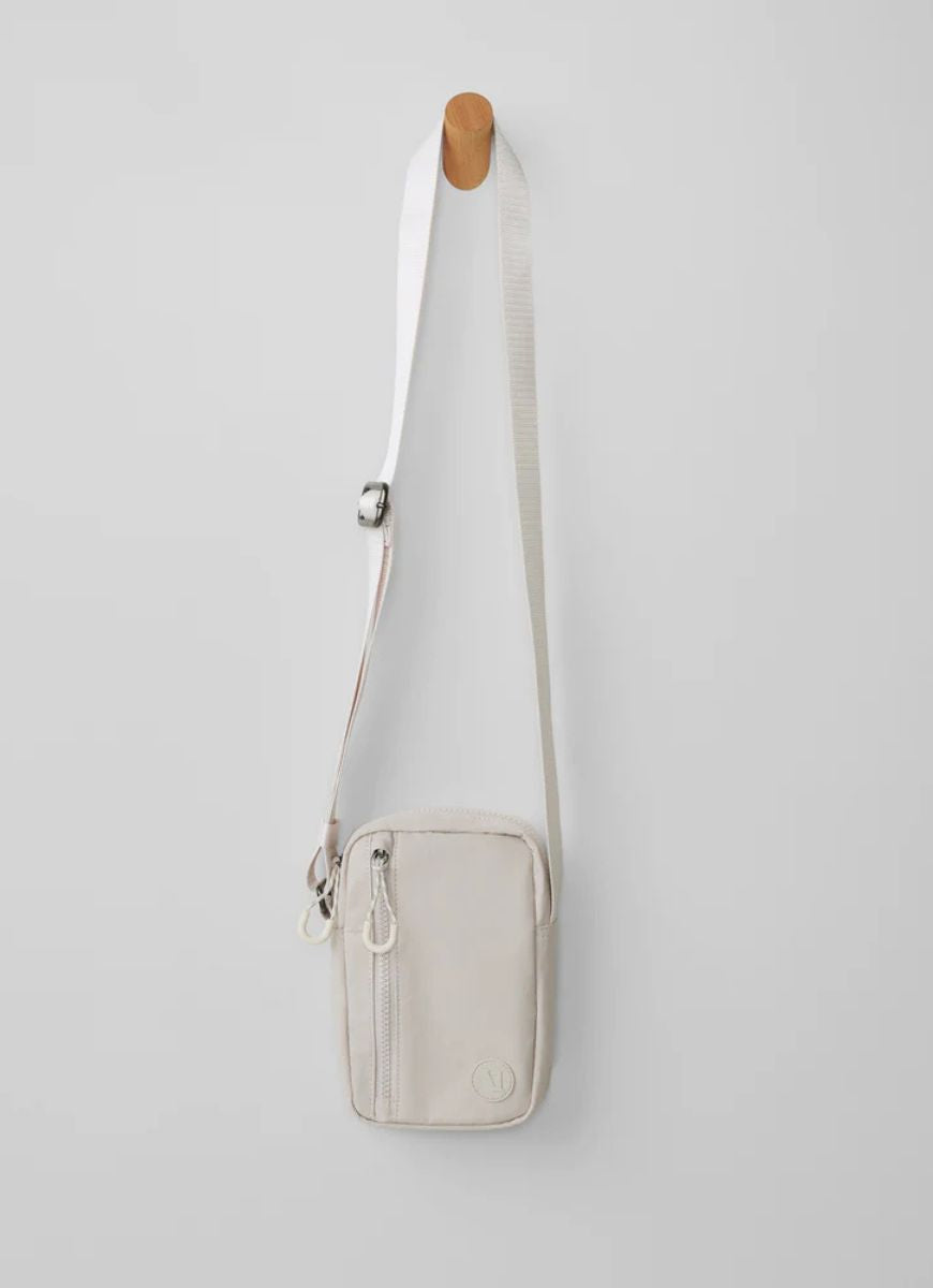 Vuori All Around Crossbody Bag in Ecru Shown Hanging on a Wooden Peg