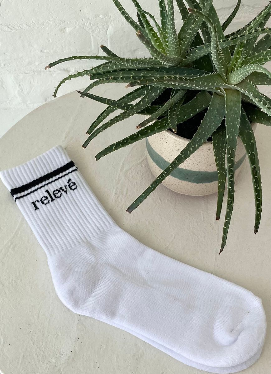 relevé Crew Socks in White with Black Logo Laying Flat on a Table