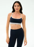 Woman wearing a black sports bra and leggings with a white stripe on a light gray background