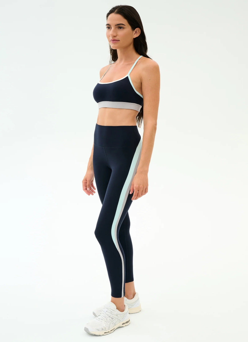 Woman wearing a black sports bra and leggings with a white stripe on a white background