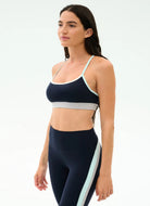 Woman wearing a navy sports bra and leggings with light blue accents on a white background