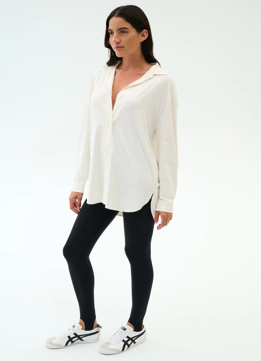 Woman wearing a white blouse, black leggings, and white sneakers on a white background