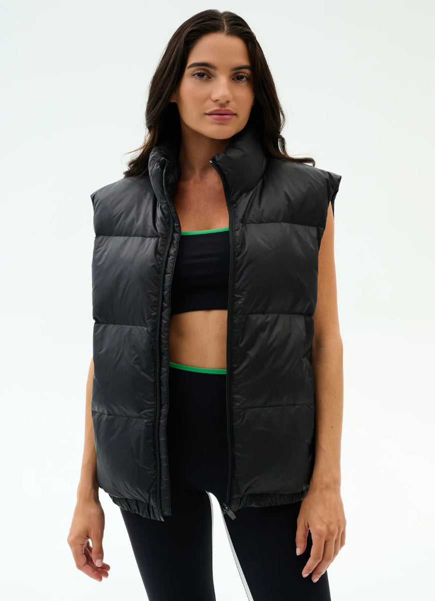 Woman wearing a black puffer vest over a sports bra and leggings on a white background