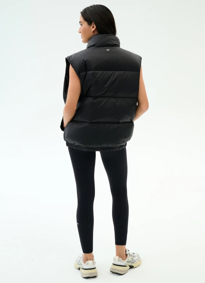 Person wearing a black puffer vest and leggings on a white background