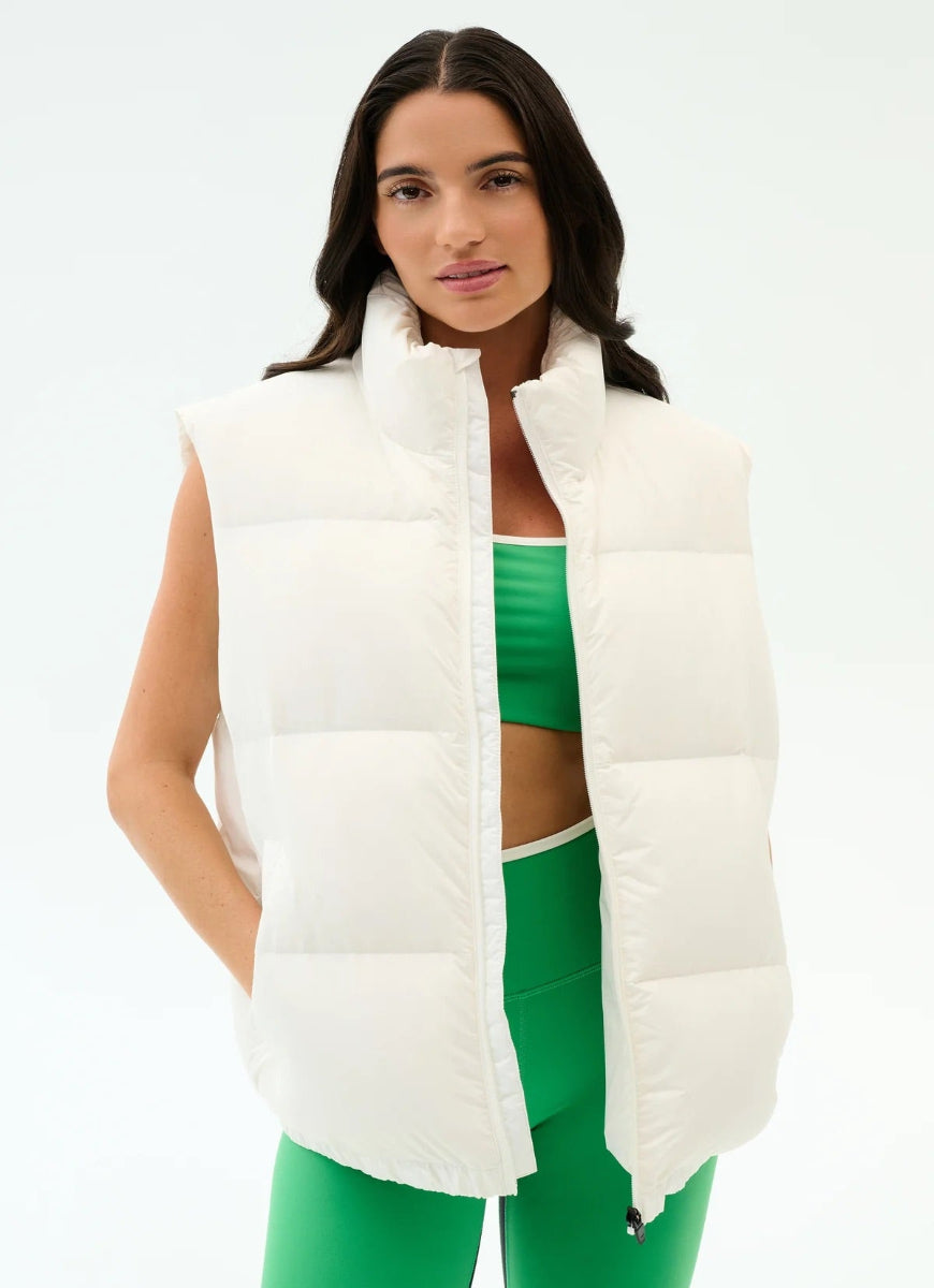 Woman wearing a white puffer vest over a green athletic outfit on a white background