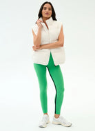 Woman wearing a white puffer vest and green leggings on a white background