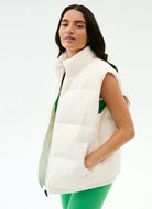 Woman wearing a white puffer vest over a green top on a light gray background