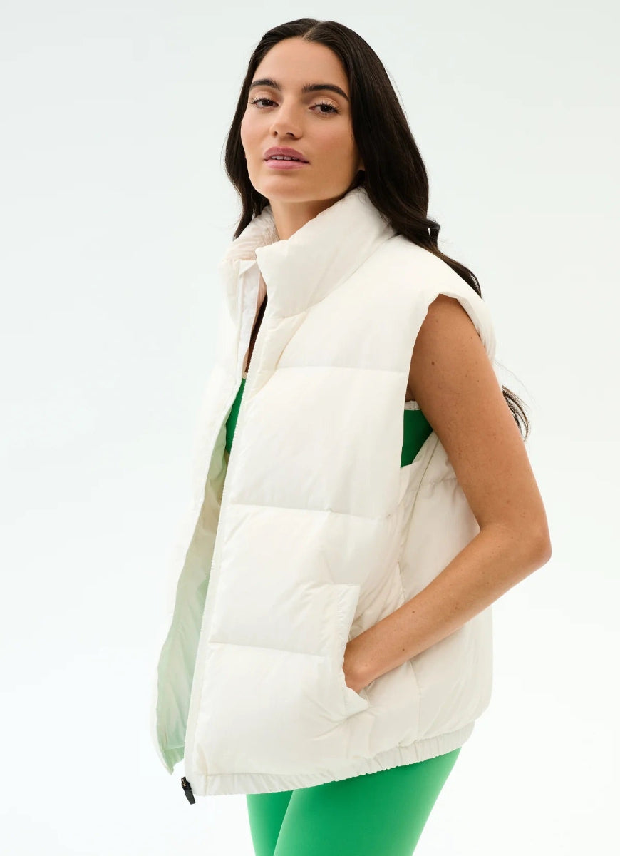 Woman wearing a white puffer vest over a green top on a light gray background