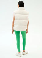 Person wearing a white puffer vest and green leggings on a white background