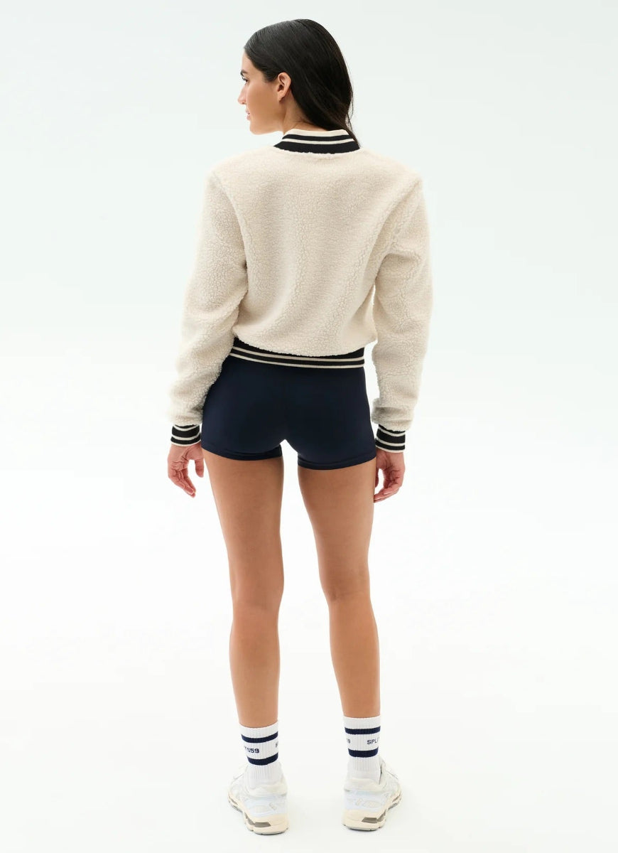 Person wearing a cream sweater with black and white striped trim, navy shorts, and white shoes on a white background