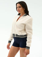 Woman wearing a white cardigan with black trim and navy shorts on a light gray background