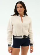 Woman wearing a white zip-up jacket with black trim and navy shorts on a white background