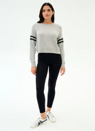 Woman wearing a gray sweater with black stripes and black leggings on a white background