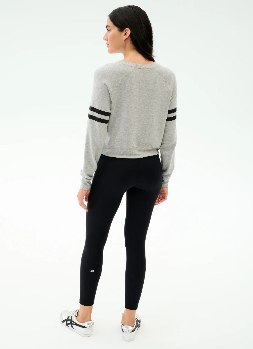 Woman wearing a gray sweater with black stripes and black leggings on a white background