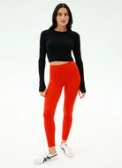 Woman wearing black long-sleeve top and red leggings on a white background