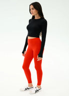 Woman wearing black long-sleeve top and red leggings on a white background