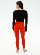 Person wearing black long-sleeve top and red leggings on a white background