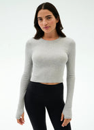 Woman wearing a gray long-sleeve crop top and black leggings on a white background