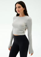 Woman wearing a gray long-sleeve crop top and black leggings on a white background