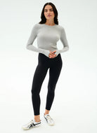 Woman wearing a gray long-sleeve top and black leggings on a white background