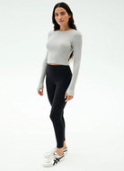 Woman wearing a gray long-sleeve top and black leggings on a white background
