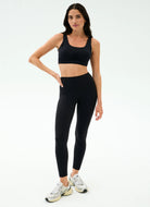 Woman wearing a black sports bra and leggings set on a white background