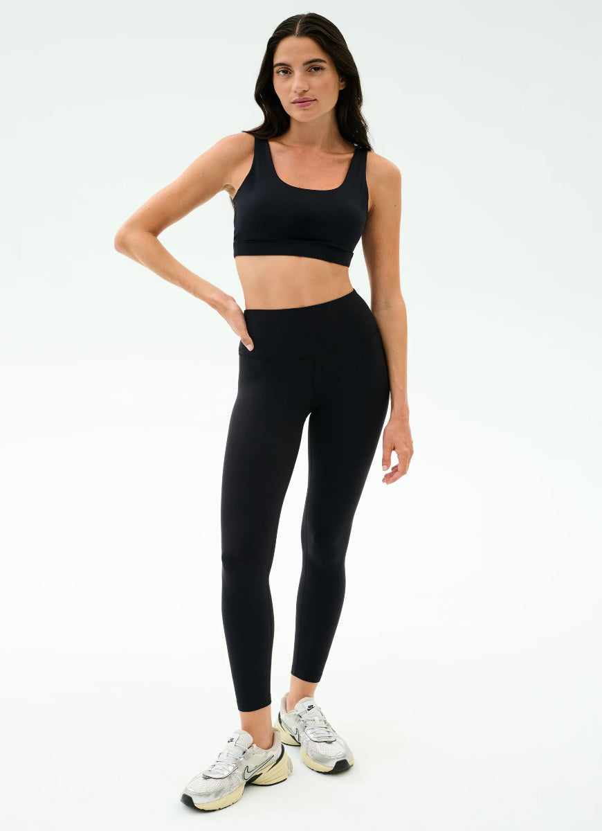 Woman wearing a black sports bra and leggings set on a white background