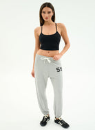 Woman wearing a black sports bra and gray sweatpants with '59' on a white background